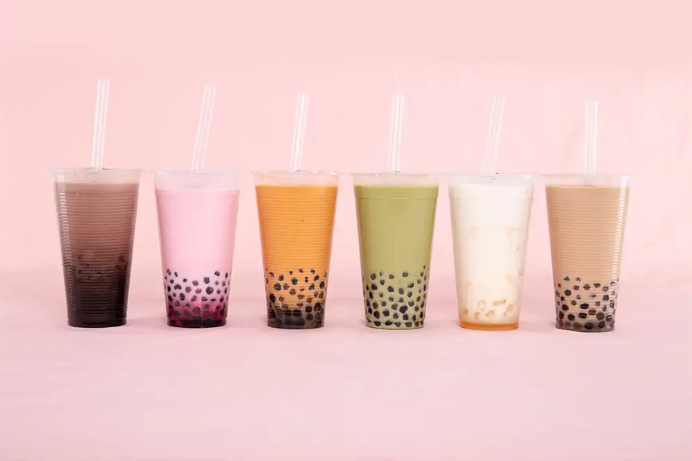 A row of colorful bubble tea cups: taro, strawberry, brown sugar, matcha, milk and classic milk tea